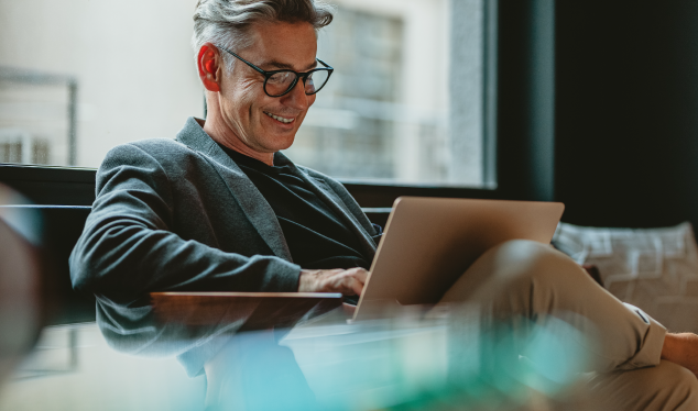 Homem sorridente a trabalhar num portátil num ambiente moderno e confortável, simbolizando a flexibilidade e eficiência proporcionadas por soluções digitais e conectividade inteligente.