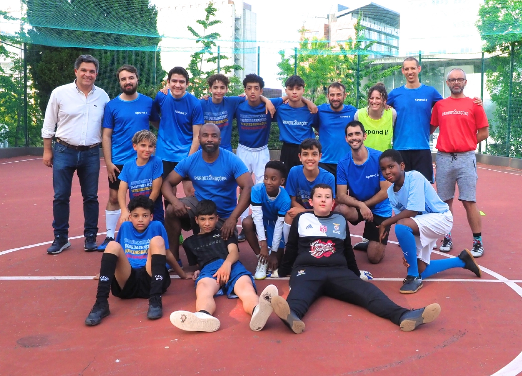 Grupo de jovens e adultos posa para a foto num campo de futebol, vestem camisolas da iniciativa Parque das Nações e Xpand IT. A imagem representa inclusão social, trabalho em equipa e responsabilidade comunitária através do desporto.