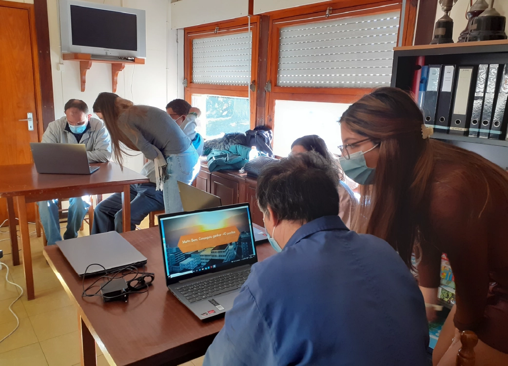 Grupo de pessoas numa sessão de formação digital, a utilizar laptops para aprender novas competências tecnológicas. A imagem representa inclusão digital, aprendizagem colaborativa e impacto social.