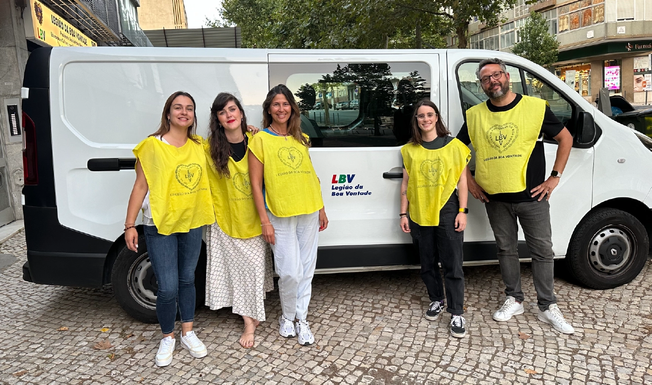 Grupo de voluntários com coletes amarelos da Legião da Boa Vontade (LBV) posa em frente a uma carrinha da organização. A imagem representa compromisso social, solidariedade e apoio comunitário.