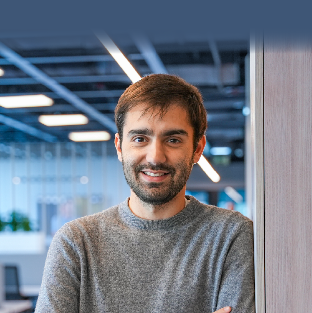 Professional portrait of a smiling man in a modern, well-lit workspace, conveying an image of technological confidence.