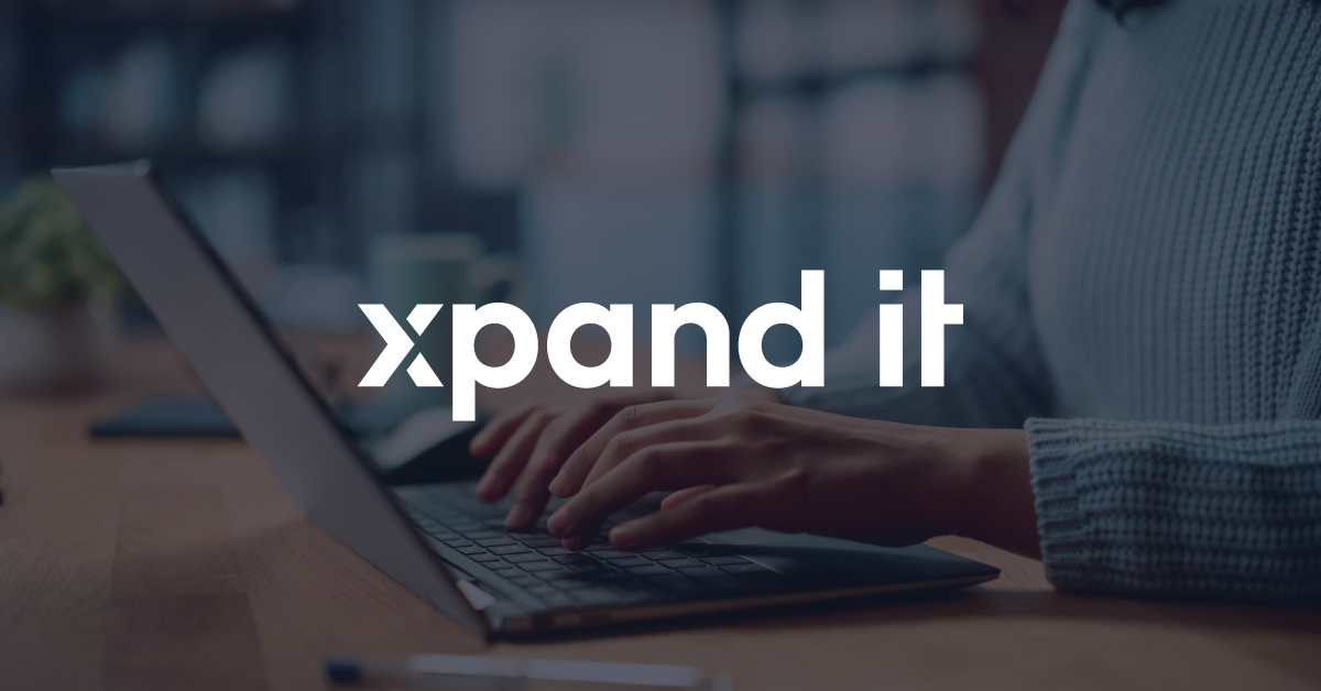 Pessoa trabalhando num laptop com o logótipo "Xpand IT" sobreposto no centro da imagem. O ambiente sugere inovação e transformação digital, refletindo um espaço de trabalho moderno e conectado.