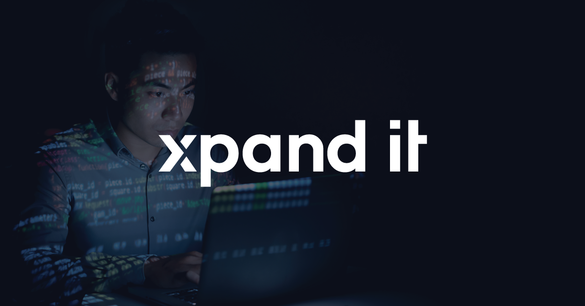Focused developer coding in a dark environment, with lines of code projected onto his face and shirt as he works on a laptop. The overlaid "Xpand IT" logo reinforces the company’s identity in a tech-driven setting.