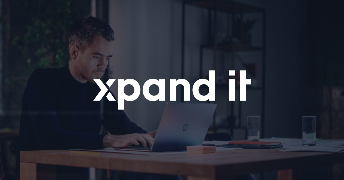 Man working intently on a laptop, with the Xpand IT logo prominently centered. The image conveys professionalism, technology, and software development.