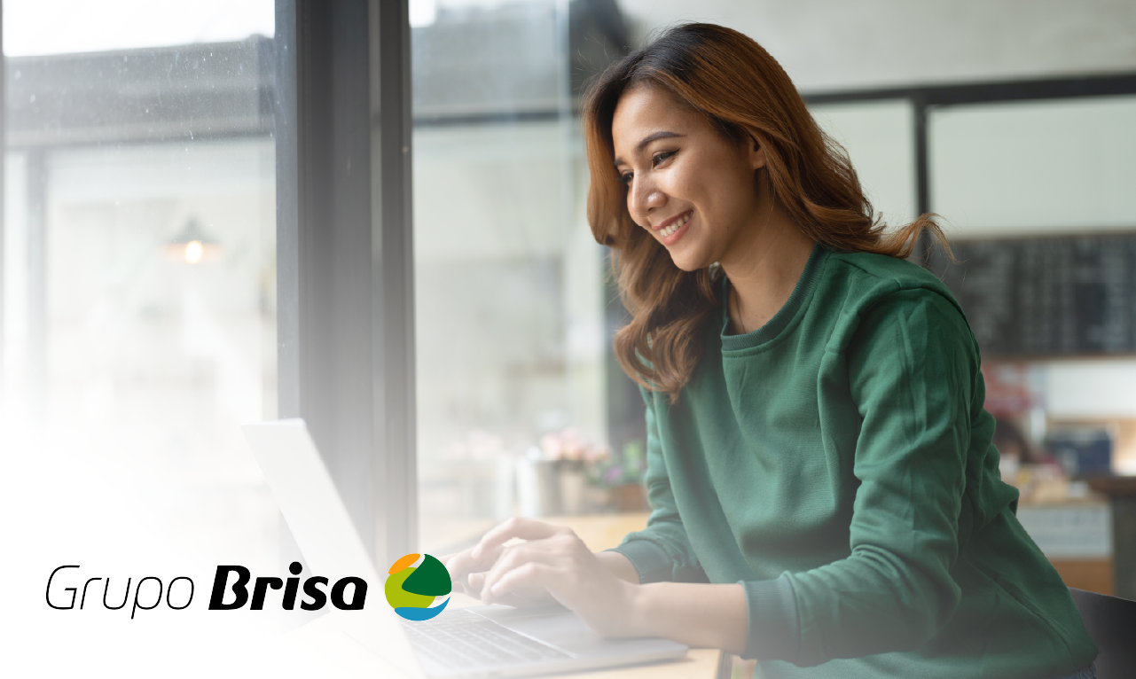 Mulher a trabalhar remotamente num ambiente descontraído, com um sorriso enquanto utiliza o portátil. O logótipo do Grupo Brisa representa inovação digital e flexibilidade no setor da mobilidade.