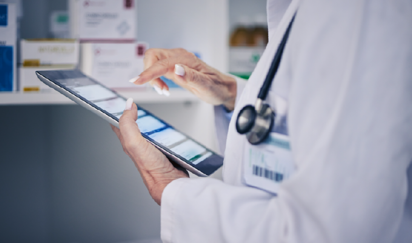 Healthcare professional in a white coat with a stethoscope uses a tablet to access digital medical data, with medication packages visible in the background. The image highlights the integration of technology in clinical practice.