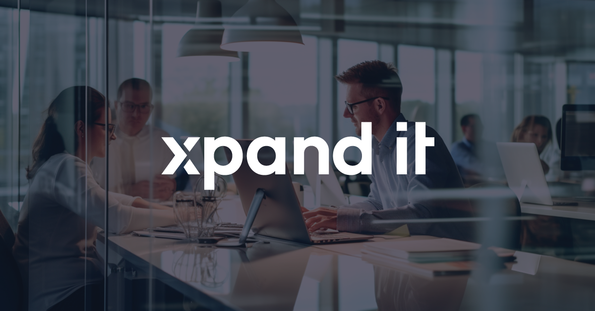 Professionals working in a modern office, collaborating on projects with laptops on a glass table. The "Xpand IT" logo is overlaid in the center, emphasizing innovation and digital transformation.