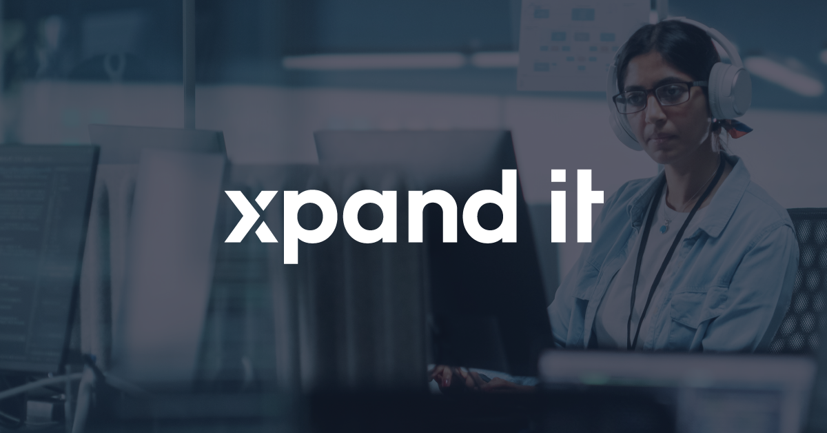 A technology professional, wearing headphones and glasses, works in a modern office environment surrounded by multiple monitors displaying code. The "Xpand IT" logo is overlaid at the center of the image.