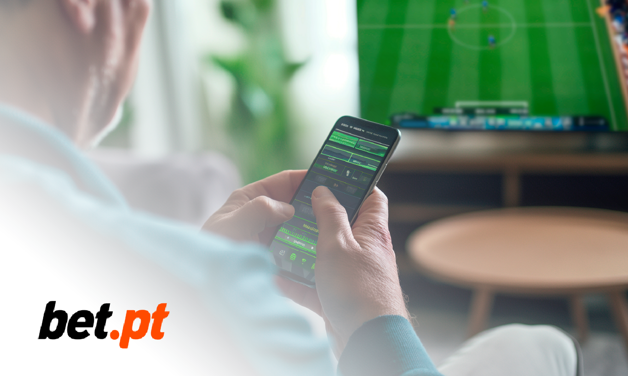 Pessoa a usar a aplicação da bet.pt no telemóvel enquanto assiste a um jogo de futebol na televisão.