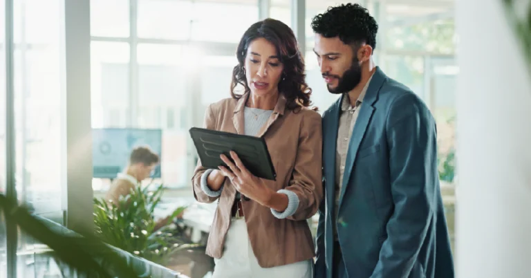 Two professionals analyzing information on a tablet in a bright, modern office environment. The image conveys collaboration, decision-making, and digital support in a corporate context.