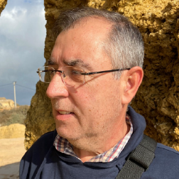 Man with glasses in an outdoor setting, near rock formations.