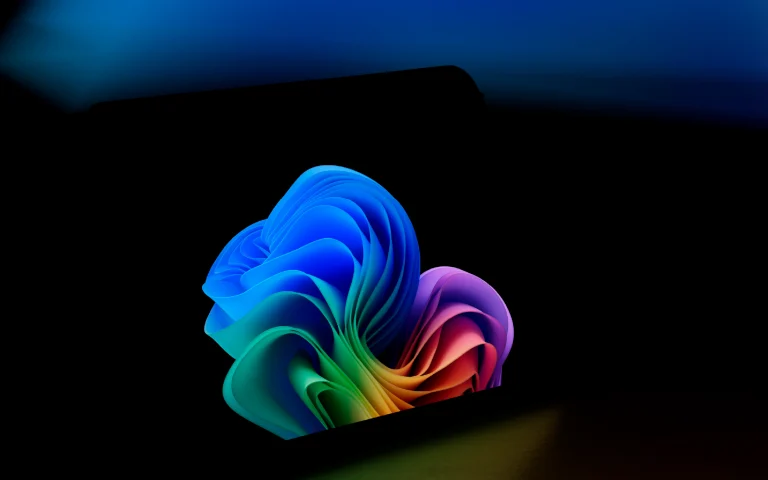 Imagem abstrata de uma forma 3D colorida que combina tons de azul, verde e rosa, destacando-se contra um fundo escuro e com brilho suave, sugerindo inovação tecnológica.
