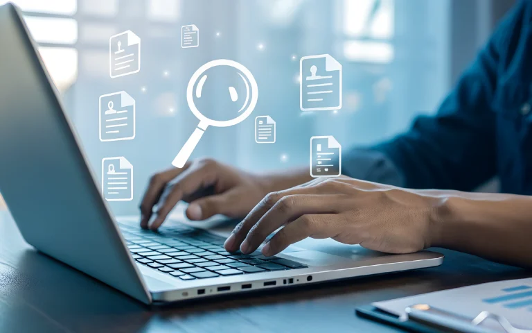 Hands typing on a laptop with overlaid digital icons including a magnifying glass and documents.