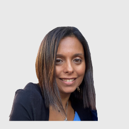 Woman with straight dark hair smiling, wearing a black blazer and blue blouse against a neutral background.
