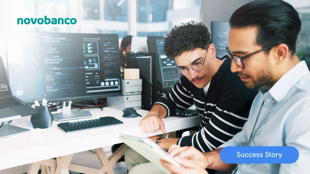 Two professionals analyze data on a tablet in front of code-filled screens in a digital development environment, featuring novobanco and a highlighted success story.