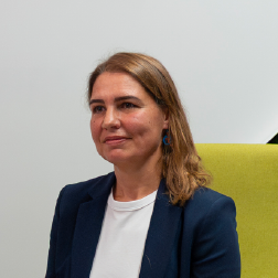 Woman with light brown hair, wearing a dark blue blazer and white blouse, seated on a green chair in a professional setting.