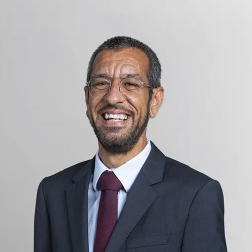 Retrato de Carlos Coelho, da Morais Leitão, de fato escuro e gravata vermelha, a sorrir para a câmara sobre um fundo neutro.
